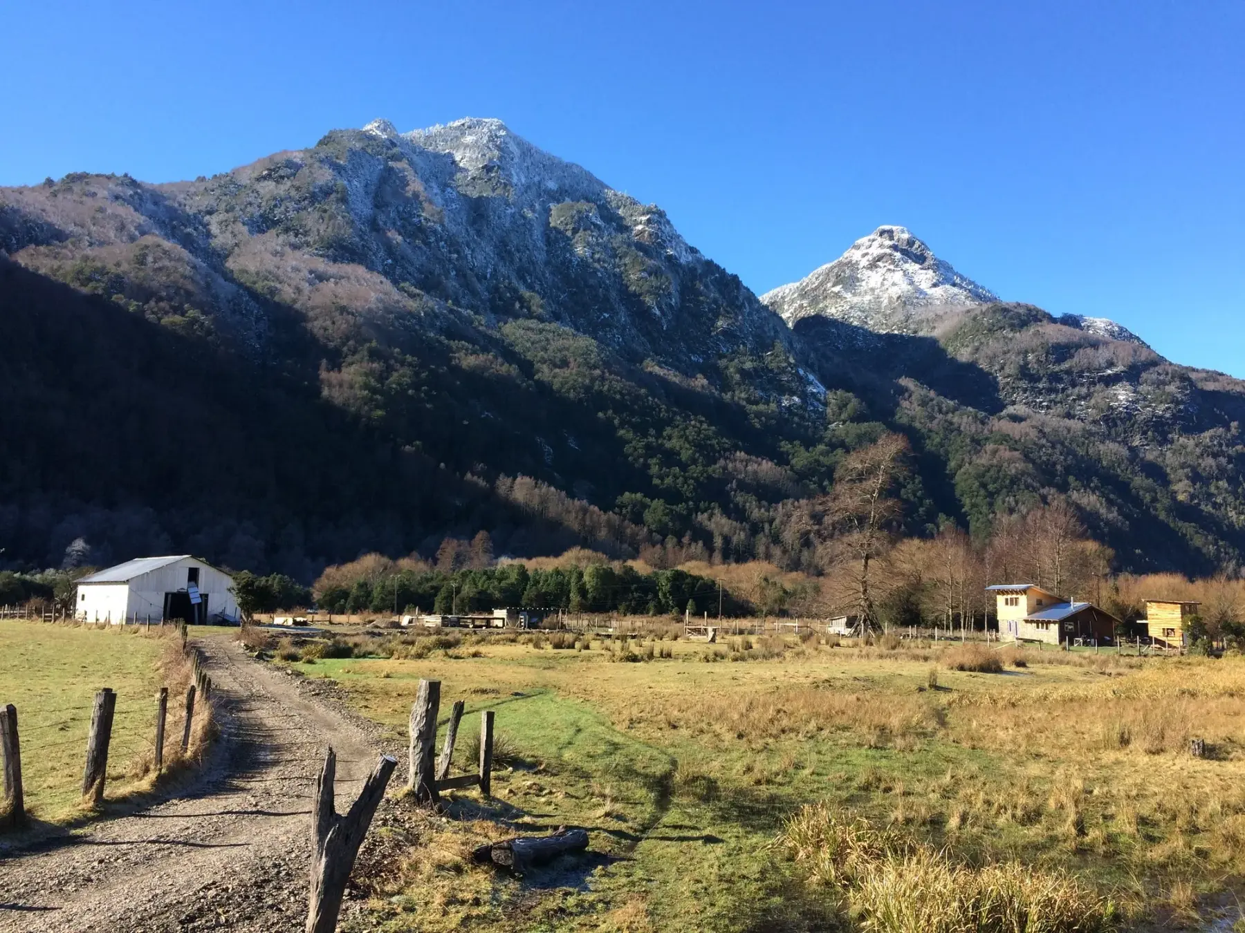 Camino rural de Curarrehue junto al río Trancura, con cerros nevados y casas de campo