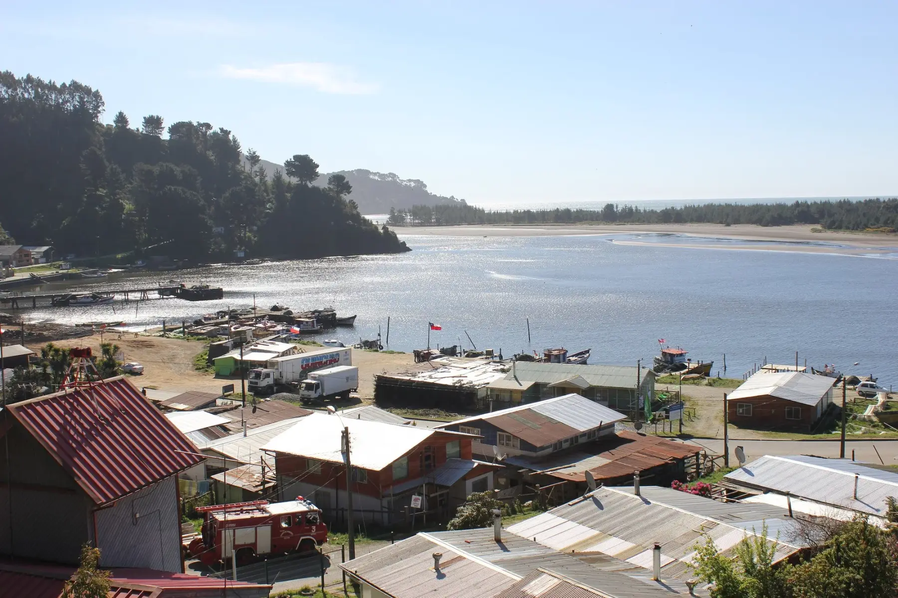 Caleta Queule en Toltén: casas del pueblo, botes en el río y la desembocadura al mar al fondo